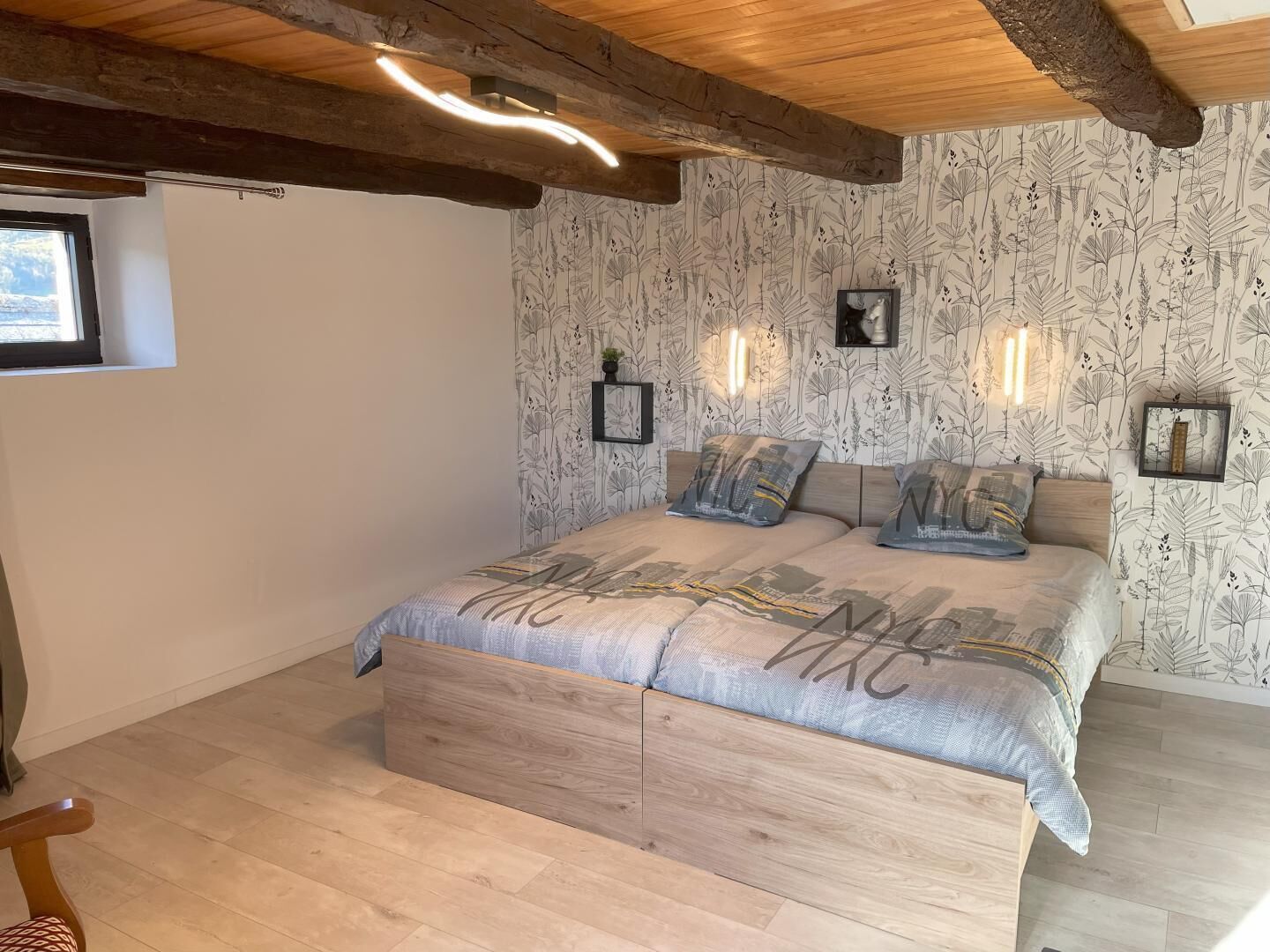 Une chambre avec un plafond en bois, un lit avec une literie à motifs, des lampes fixées au mur et une fenêtre.