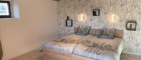 Une chambre avec un plafond en bois, un lit avec une literie à motifs, des lampes fixées au mur et une fenêtre.