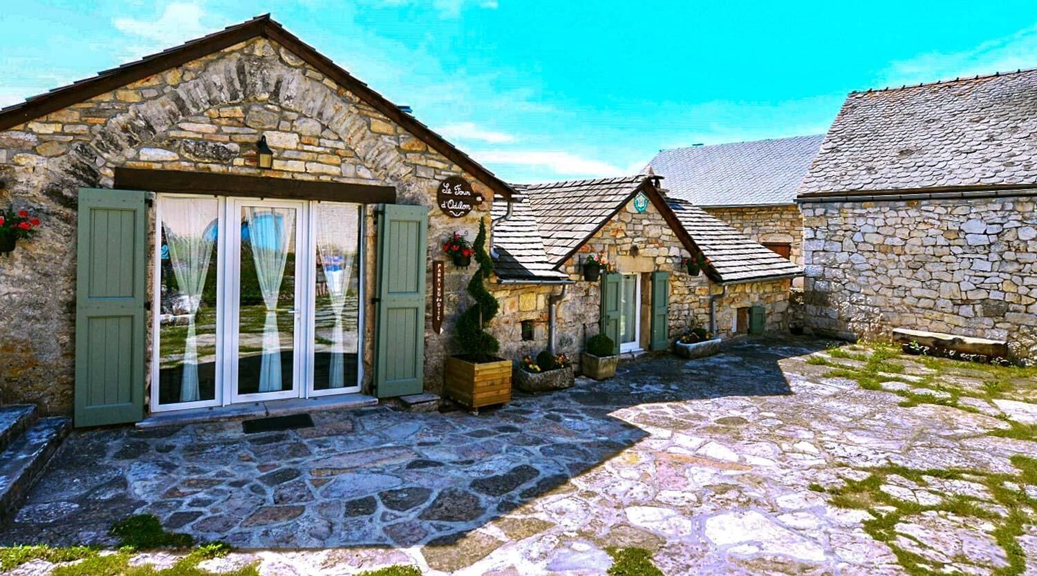 Un edificio de piedra con un cartel que dice 'La Maison des Vignerons', un patio empedrado y un pequeño jardín.