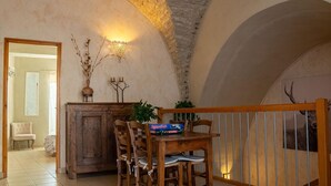A rustic dining area with a wooden table and chairs, a stone wall, and a staircase leading to a balcony. - Le Four d'Odilon 6 people in Montignac (MALENE (LA))
