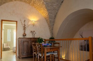 Ein rustikaler Essbereich mit Holztisch und -stühlen, einer Steinwand und einer Treppe zu einem Balkon.