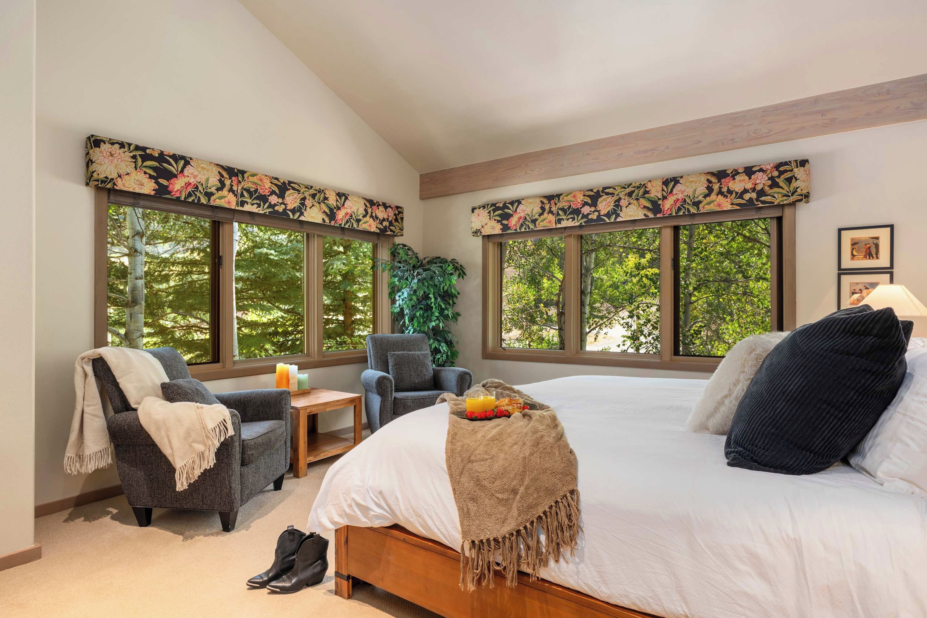 Une chambre à coucher avec un grand lit, deux fauteuils, une petite table et une fenêtre donnant sur des arbres.