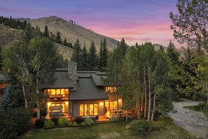 A two-story lodge with a stone chimney, a deck, and a view of a mountain range. - Abode at Guyer Hot Springs, ski slope views, walk to lift, hot tub (Ketchum)
