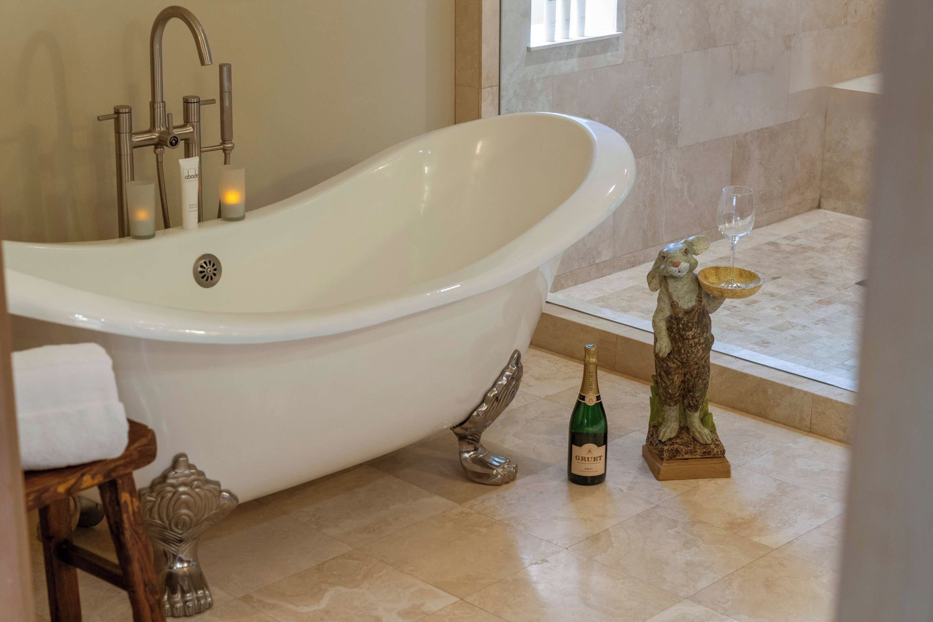 Une salle de bain avec une baignoire sur pieds, une bouteille de champagne Gruet et une figurine de lapin en céramique.