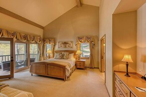 A bedroom with a large bed, a nightstand, a dresser, and a window with curtains.