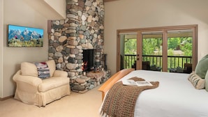 A bedroom with a stone fireplace, a sofa, a bed, and a balcony with a view of greenery. - Abode at Guyer Hot Springs, walk to lift, hot tub (Ketchum)