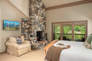 A bedroom with a stone fireplace, a sofa, a bed, and a balcony with a view of greenery. - Abode at Guyer Hot Springs, walk to lift, hot tub (Ketchum)