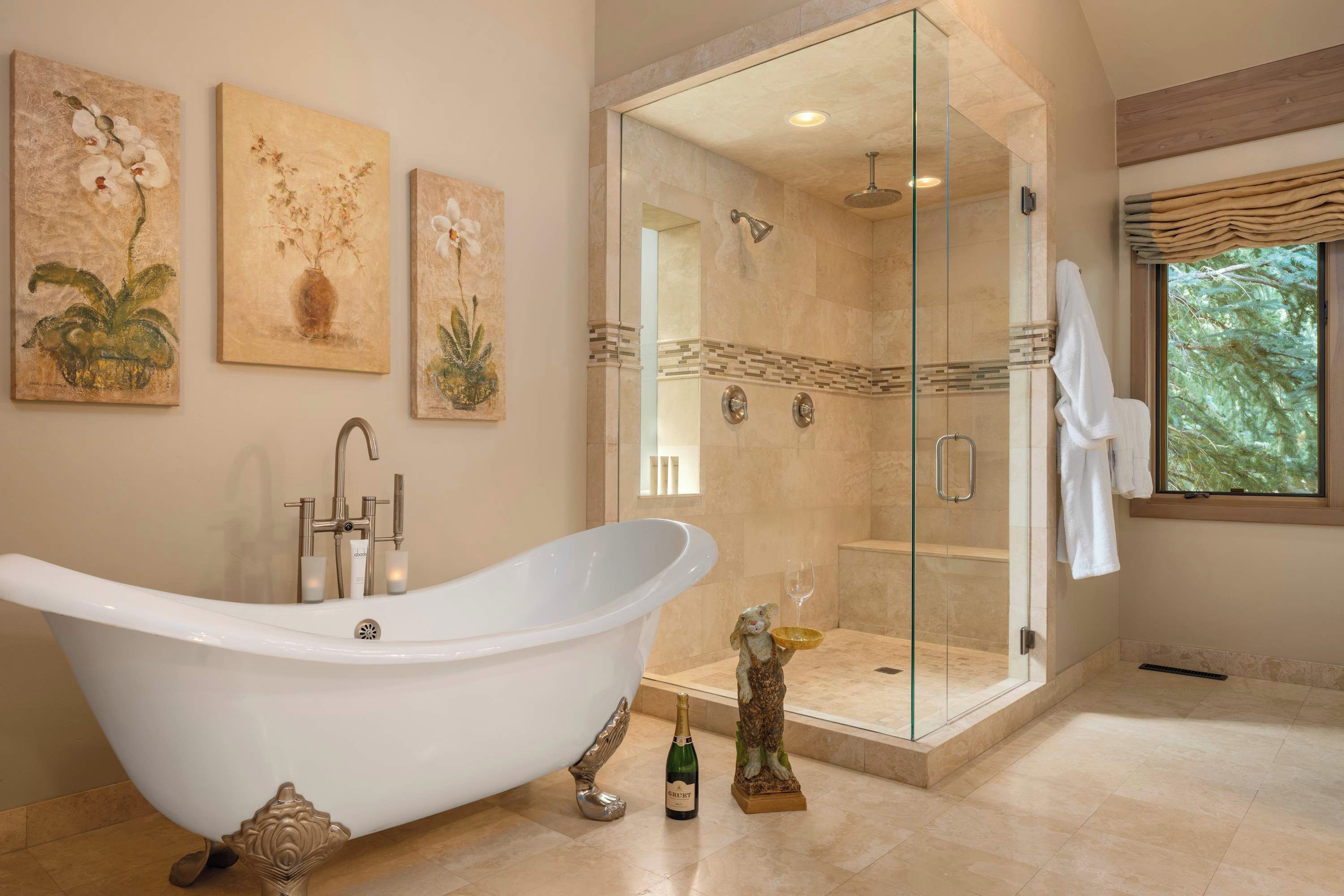 Een badkamer met een vrijstaand bad, een douche met glazen wanden en drie wanddecoraties.