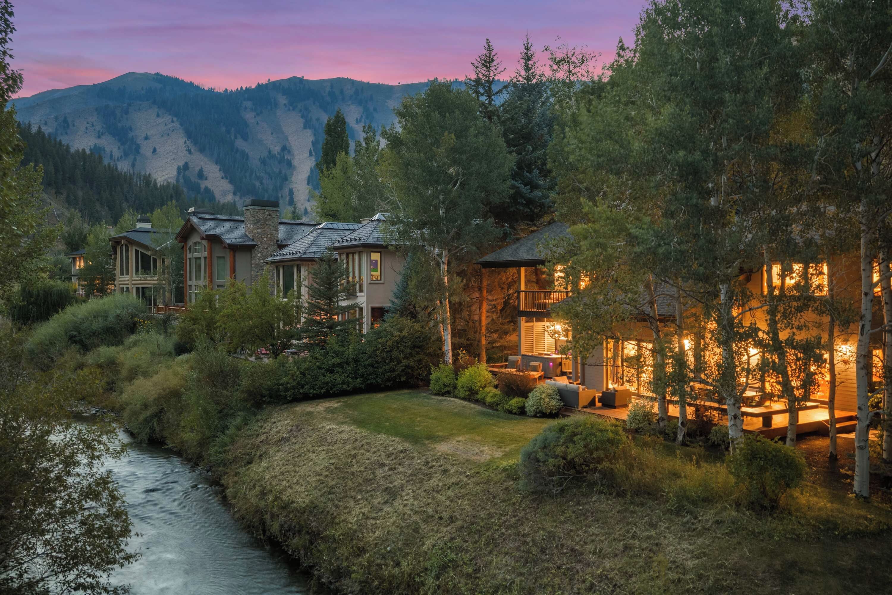 A residential area with multiple houses, a river, and mountains in the background.