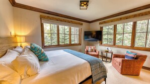 Un dormitorio con cama, una silla, un televisor y ventanas amplias.