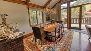 Un comedor con mesa de madera, sillas, una lámpara de araña y vistas al exterior.