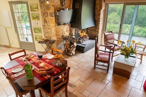 A dining area with a stone wall, a fireplace, and a TV mounted on the wall. - Gîte de Pratpanoul 3 épis 4/6 pers in Quézac (QUEZAC)