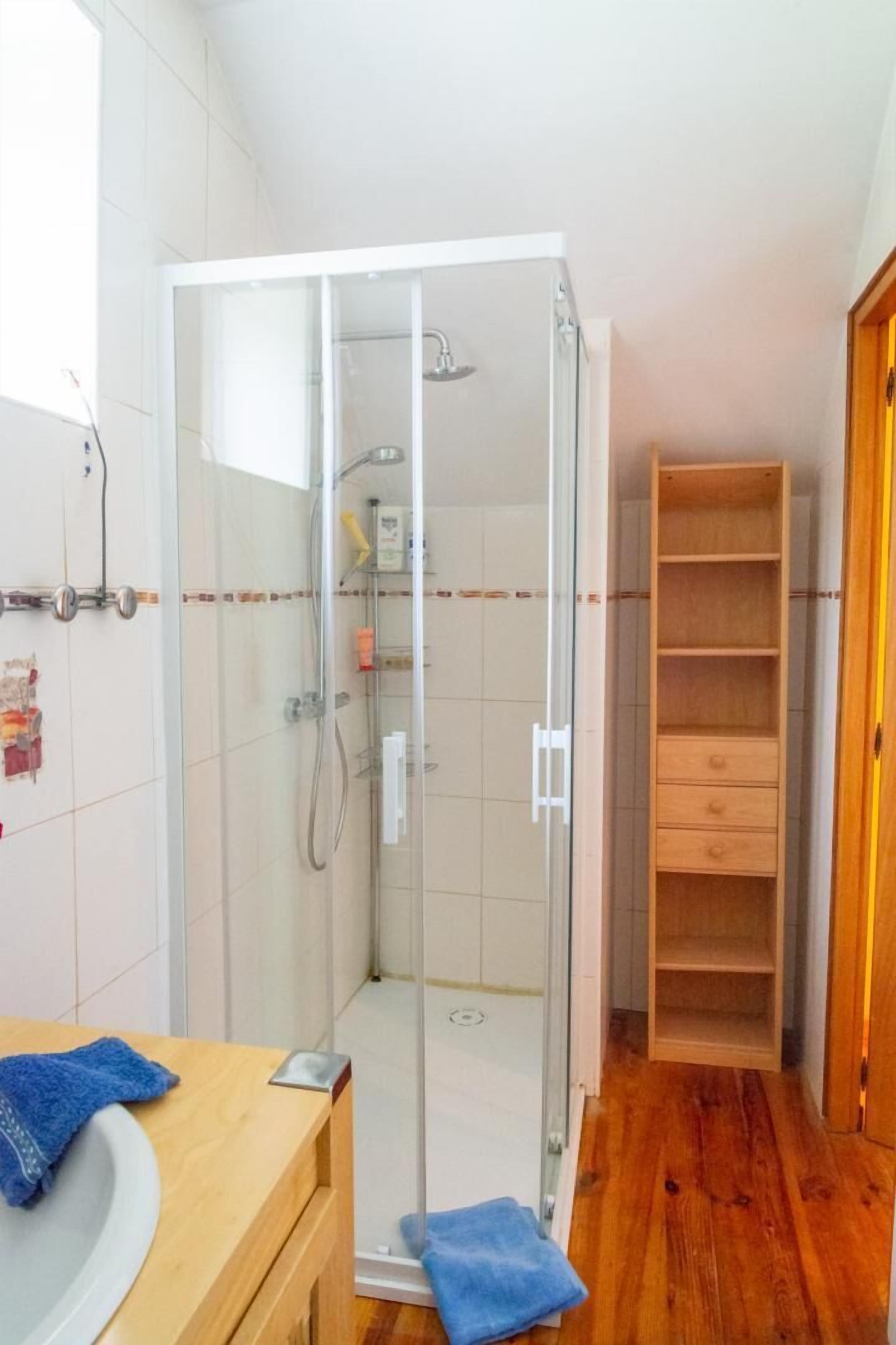 Une salle de bain dotée d’une douche à parois de verre, d’un meuble-lavabo en bois et d’une étagère intégrée.