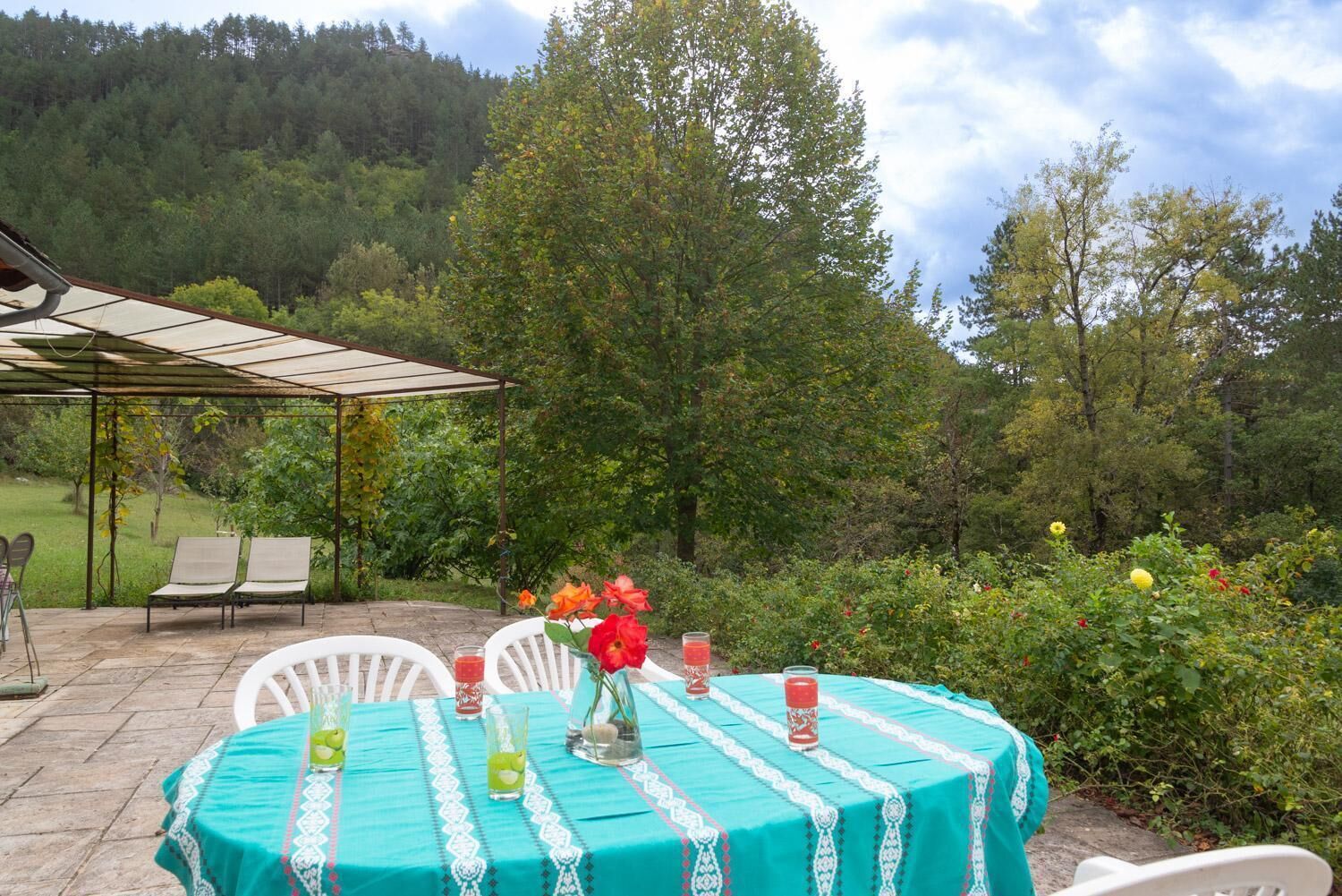 Un patio al aire libre con una mesa preparada para dos personas, rodeado de follaje y árboles.