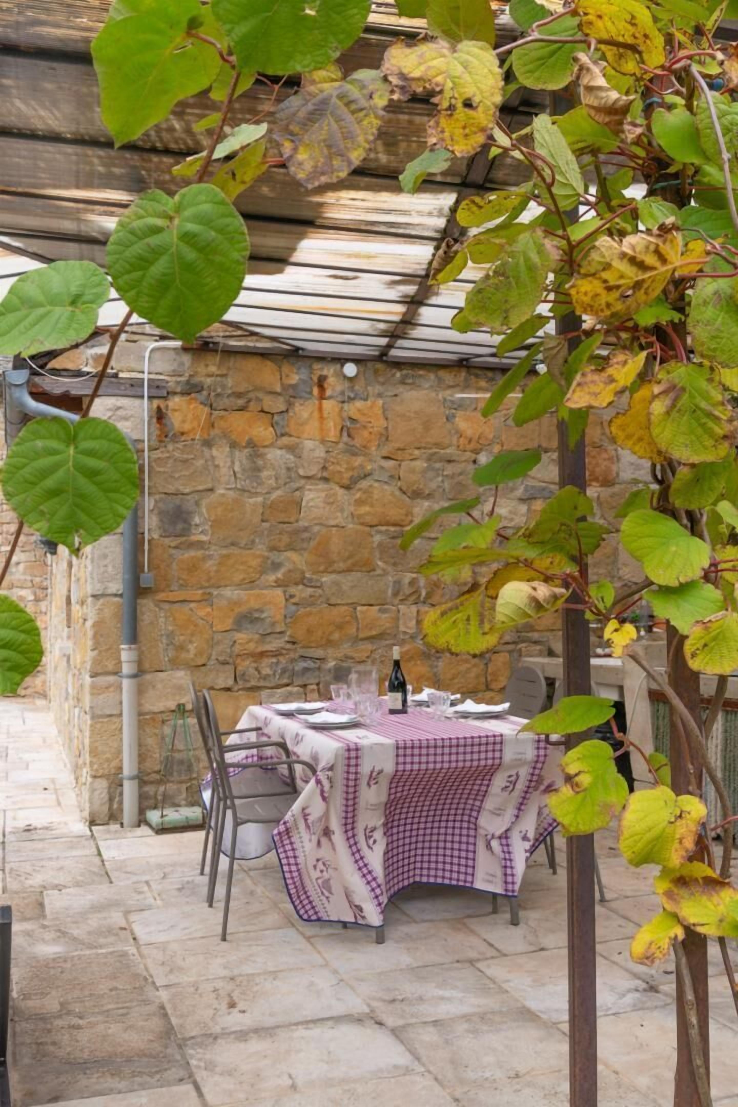 A stone wall, a table with a checkered tablecloth, and chairs.