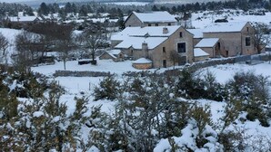 En stenbyggnad på landsbygden med flera skorstenar, omgiven av snötäckta träd och ett kuperat landskap.