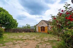 A stone building with a wooden door and window shutters, surrounded by a stone wall and a garden with red roses. - Gîte de Dignas 2/4 persons (SAINTE-ENIMIE)