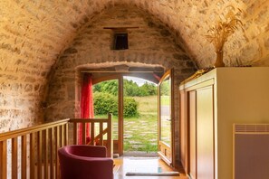Una habitación de piedra con arco, con una silla de madera, una mesita y un armario.