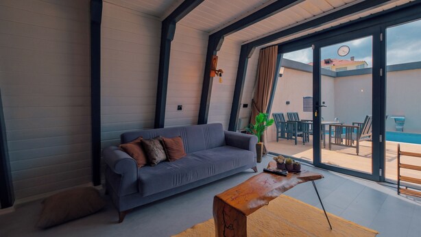 Una sala moderna con un sofá gris, una mesa de centro de madera y un gran ventanal corredero que da a un área exterior con piscina.