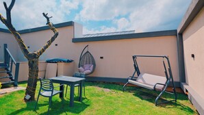 Un patio con mesa, sillas, un columpio, una hamaca colgante y un árbol envuelto en cuerda.