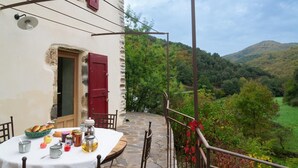 Ein Steintisch mit Frühstücksangeboten, eine rote Tür und Blick auf ein grünes Tal.