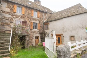 Ein Steinhaus mit einem kleinen Balkon, einer Holztür und einem weißen Zaun.