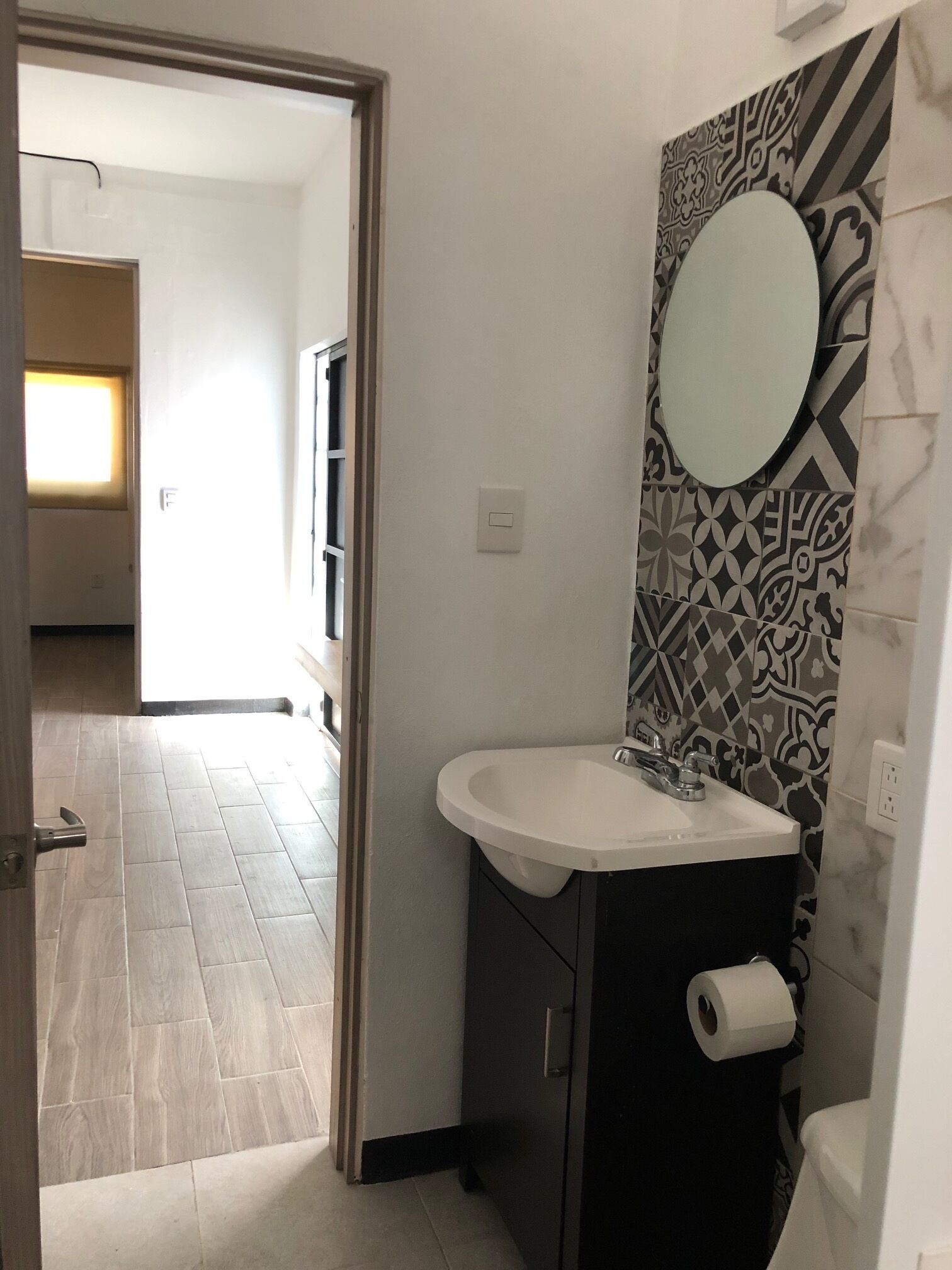 Un baño con un lavabo blanco, un espejo, azulejos estampados y un inodoro.