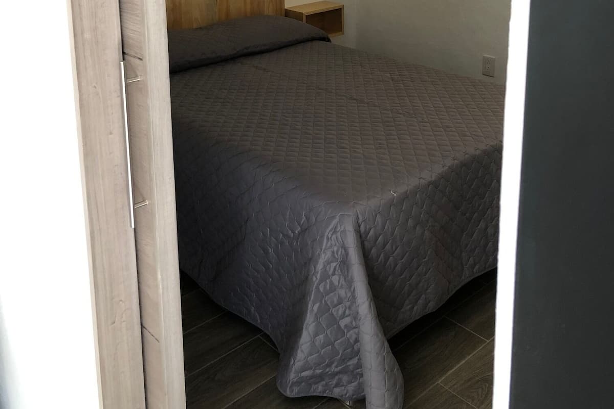 A bedroom with a bed, wooden headboard, bedside table, and a window with natural light.