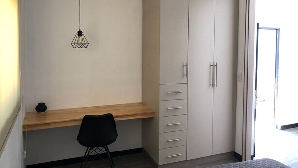 A bedroom with a bed, a desk with a chair, a wardrobe, and a hanging light fixture. - Casa Maye (Oaxaca)