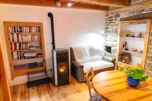 A cozy room with a wood-burning stove, a bookshelf, a sofa, and a dining table. - LA MAISON DE JULIETTE (LES SALELLES)