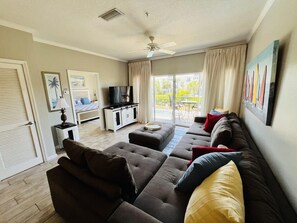 Ein Wohnzimmer mit einer Couch, einem Fernseher und einem Balkon mit Gartenmöbeln.