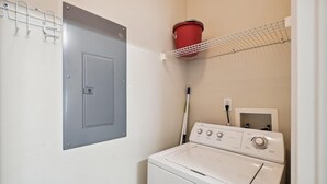 Ett tvättrum med en tvättmaskin, en torktumlare, en metalldörr, en röd hink på en hylla och en mopp.