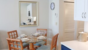 Zona pranzo con tavolo rotondo in vetro, sedie in legno, uno specchio, una sveglia e un armadietto con un asciugamano.