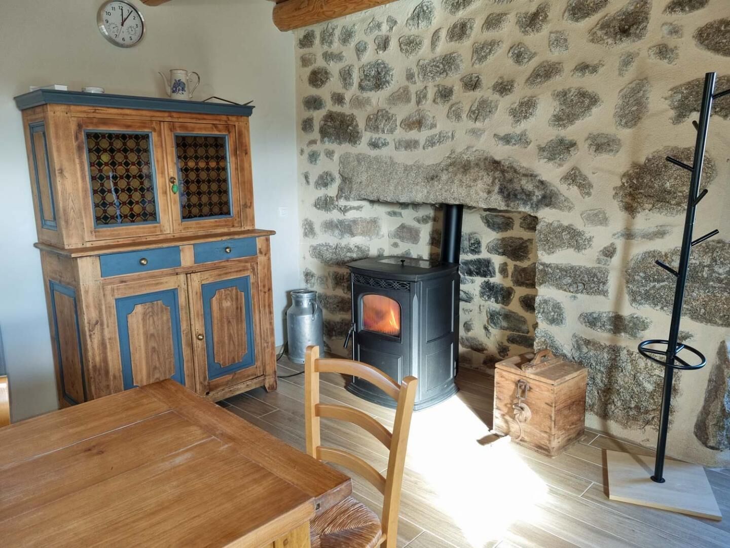 Un intérieur rustique avec un mur en pierre, une table en bois, un buffet aux portes vitrées et un poêle à bois.