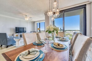 A dining area with a wooden table set for four, a television in the background, and a balcony with a view. - Enclave 701a- Shore Fun (Destin)