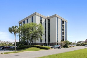 A modern building with a flat roof, large windows, and a parking lot with cars and a palm tree. - Enclave 701a- Shore Fun (Destin)