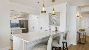 A modern kitchen with a large island, pendant lighting, and a dining area with bar stools. - Destin Towers 151- Shore Elegance (Destin)