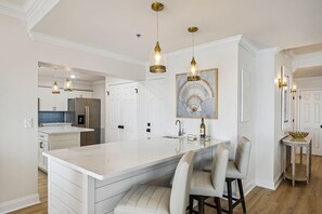 A modern kitchen with a large island, pendant lighting, and a dining area with bar stools. - Destin Towers 151- Shore Elegance (Destin)