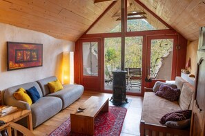 A cozy room with a wooden ceiling, a sofa, a coffee table, a fireplace, and a view of the outdoors. - EcoGîte Nature de Bieisses (QUEZAC)