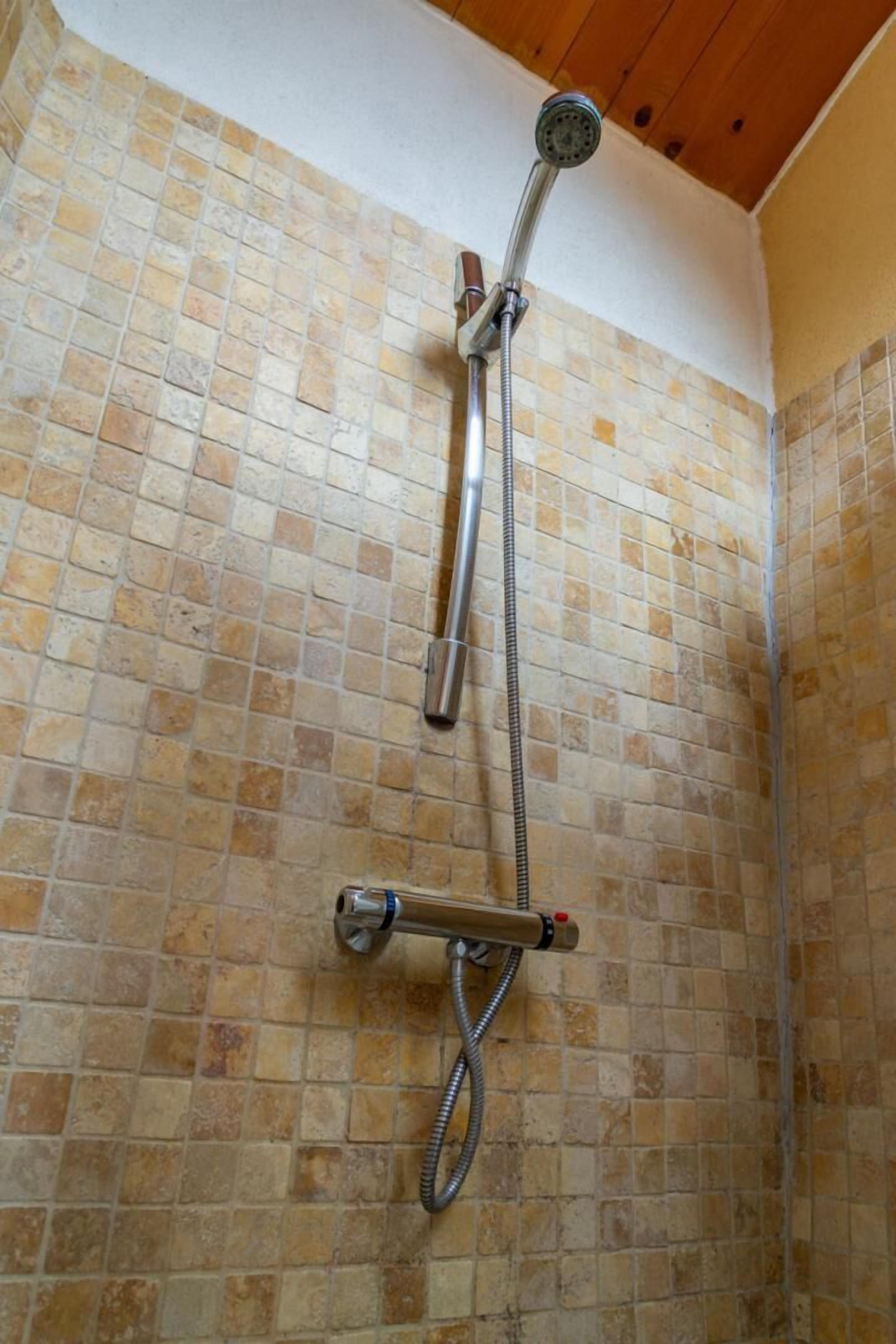 A shower with a handheld showerhead and a fixed wall-mounted showerhead, both with hoses.