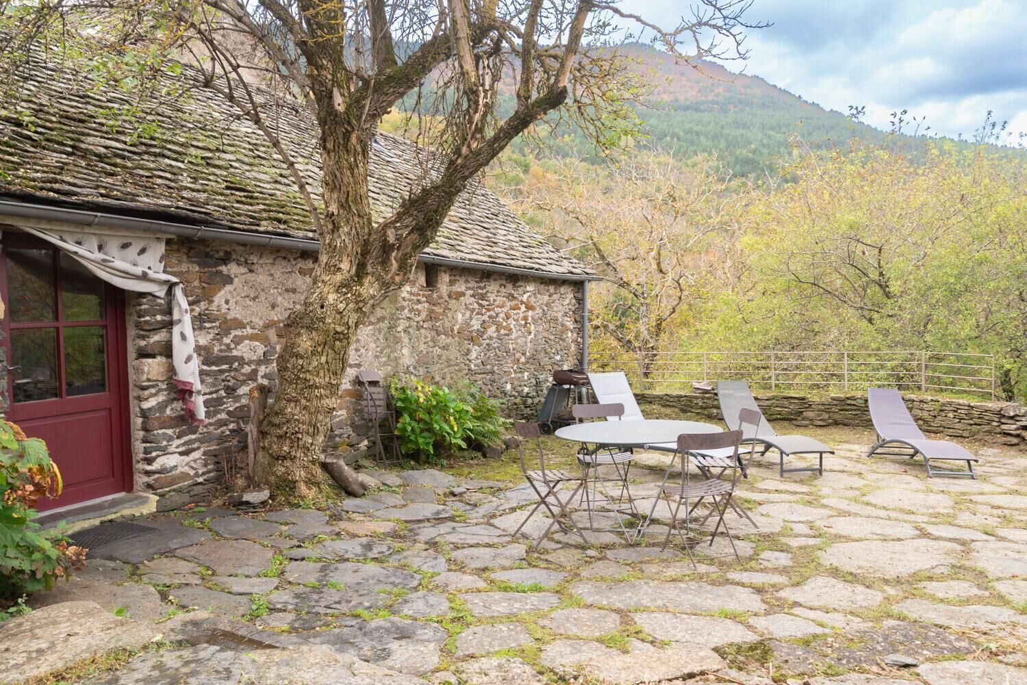 Un bâtiment en pierre avec une porte rouge, un toit en pierre et une terrasse avec une table et des chaises.