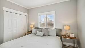 A bedroom with a bed, two bedside tables with lamps, a window with blinds, a ceiling fan, and a white door. - Emerald Waters 301- Saltwater Therapy (Miramar Beach)