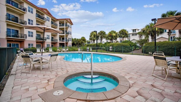 A pool area with lounge chairs and a hot tub, surrounded by a multi-story building with balconies. - Emerald Waters 301- Saltwater Therapy (Miramar Beach)