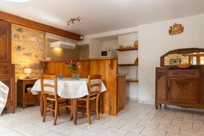 Un coin repas avec une table dressée pour quatre personnes, des chaises en bois, une nappe blanche et un vase rempli de fleurs.