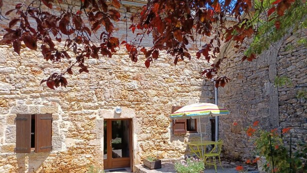 Ein Steinhaus mit einer Holztür, einem kleinen Fenster und einem Tisch mit einem Streifen-Sonnenschirm.