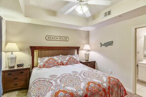 A bedroom with a bed, nightstands, a ceiling fan, a wall-mounted fish decoration, and a 'BEACH HOUSE' sign. - Destin West Gulfside 311- Paradise Gulfside (Fort Walton Beach)
