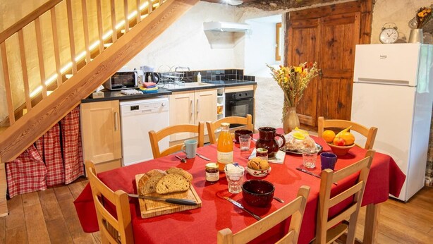 Een eethoek met een houten trap, een keuken met moderne apparatuur en een rode tafel gedekt voor een maaltijd.