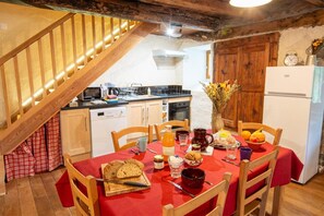 A dining area with a wooden staircase, a kitchen with modern appliances, and a red table set for a meal. - LE GITE DE GRANADE - BARJAC (BARJAC)