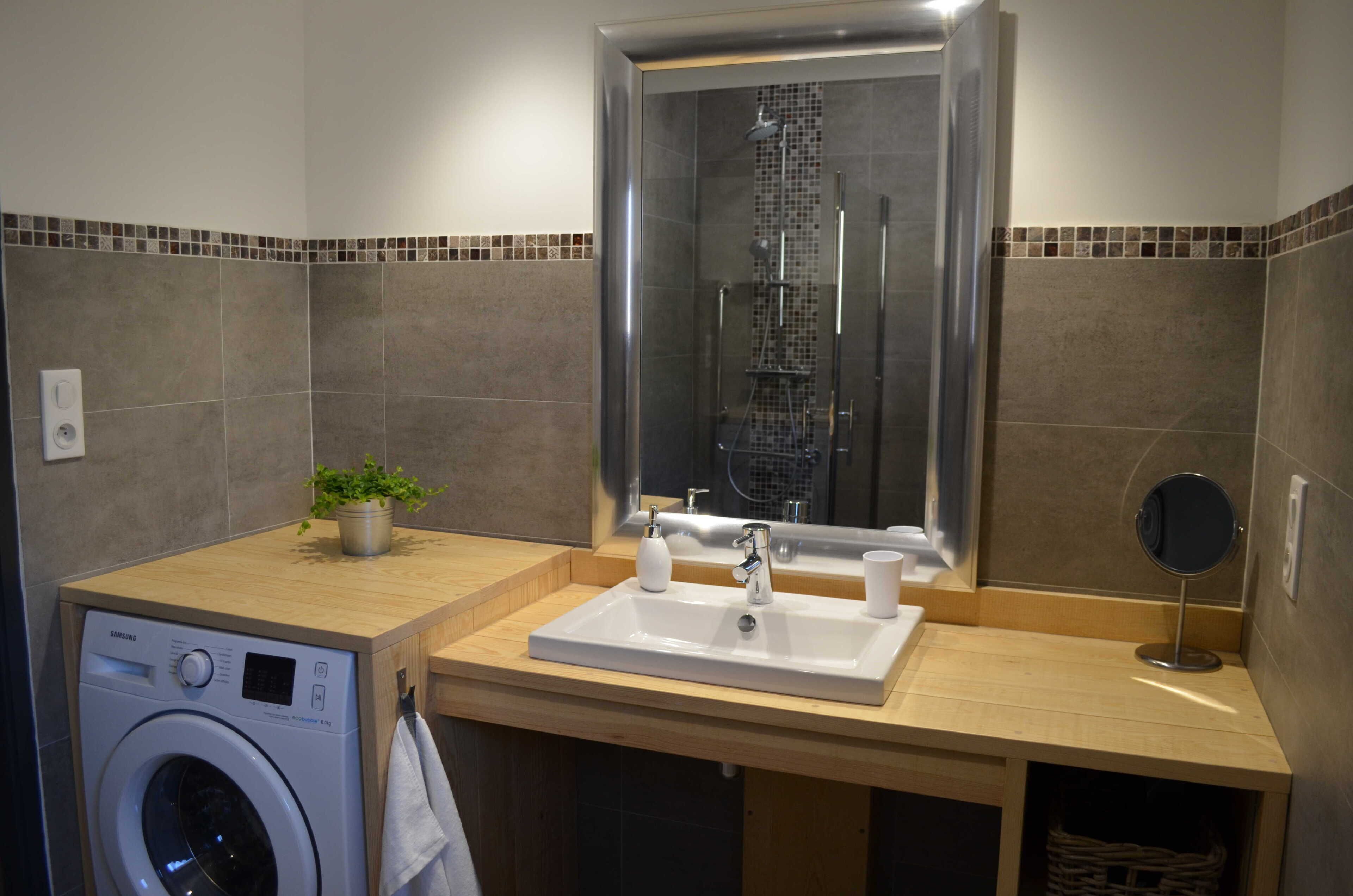 Ein Badezimmer mit Waschmaschine, Waschbecken, Spiegel und Duschkabine.