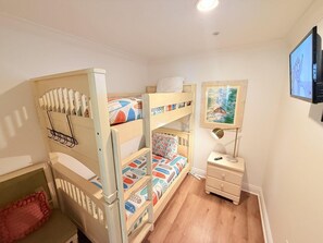 Ein Schlafraum mit Etagenbetten, einem kleinen Schreibtisch, einem gerahmten Bild an der Wand und einem an der Wand befestigten Fernseher.